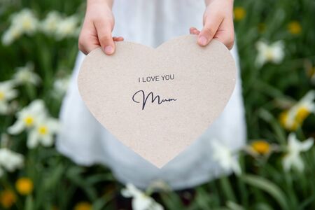 I love you mum written on a heart-shaped card held by a girl on grass backgroundの写真素材