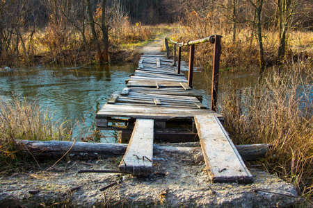 Old hand-made wooden bridge over the small river in fallの写真素材