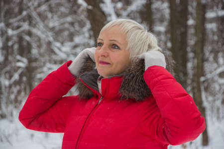 Portrait of a nice senior woman in the winter snow wood in red coatの写真素材