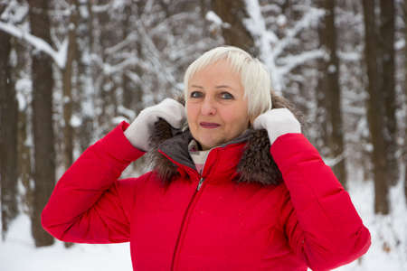 Portrait of a nice senior woman in the winter snow wood in red coatの写真素材