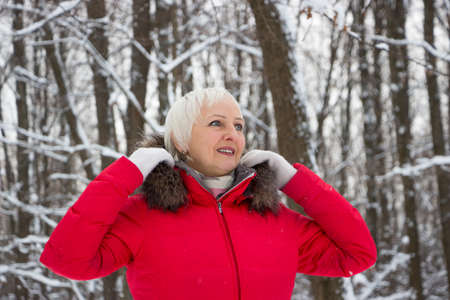 Portrait of a nice senior woman in the winter snow wood in red coatの写真素材