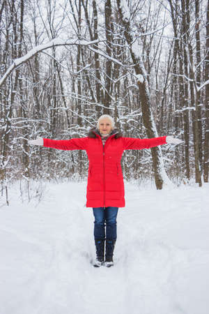 Portrait of a nice senior woman in the winter snow wood in red coatの写真素材