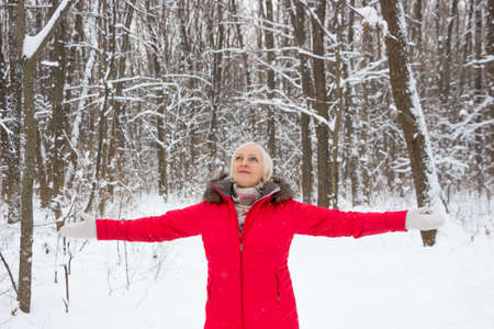 Portrait of a nice senior woman in the winter snow wood in red coatの写真素材