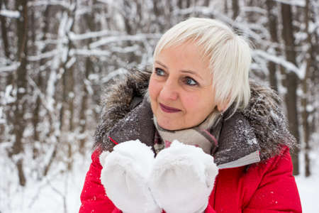 Portrait of a nice senior woman in the winter snow wood in red coatの写真素材