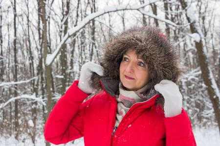 Portrait of a nice senior woman in the winter snow wood in red coatの写真素材