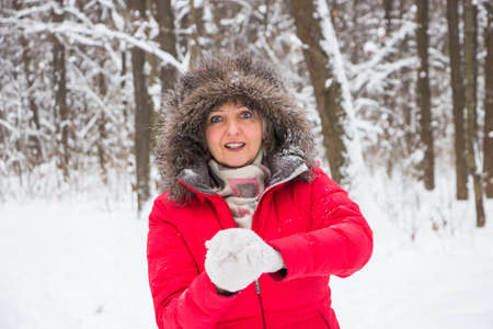 senior old woman throws snowball in the wood in red coatの写真素材