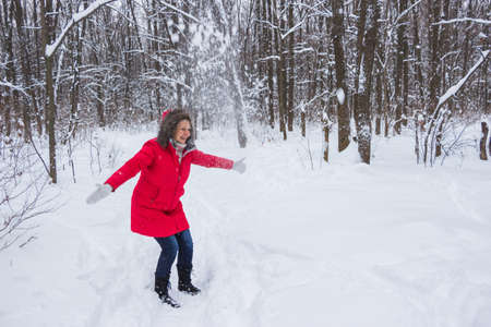 senior old woman throws snow in the wood in red coatの写真素材