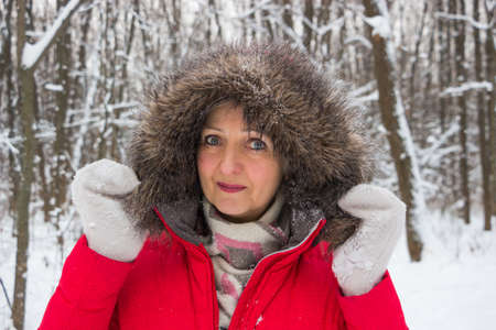 Portrait of a nice senior woman in the winter snow wood in red coatの写真素材