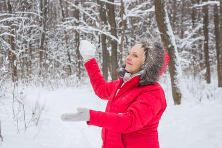 senior old woman throws snowball in the wood in red coatの写真素材