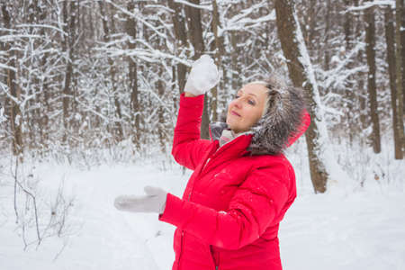 senior old woman throws snowball in the wood in red coatの写真素材
