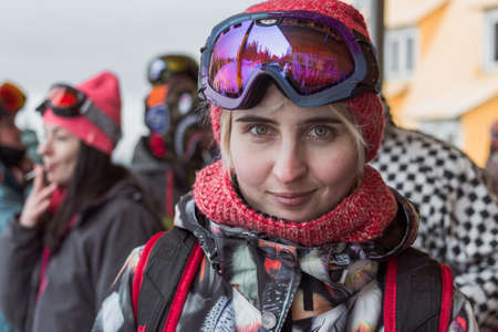 Snowboard pretty blonde girl portrait with green eyes wearing purple mask and orange hat with scarf looking forward.の写真素材