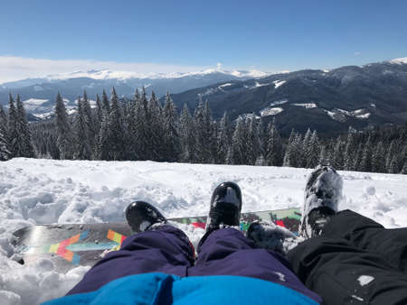 Leisure vacation in mountains on the ski report. Legs of the couple boy and girl in front of the beautiful snow mountains view.の写真素材