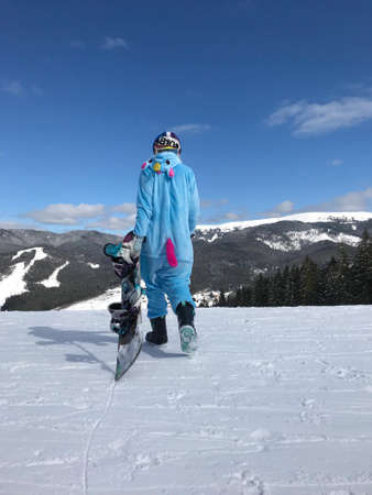 Girl in blue, pink unicorn pajama kigurumi outdoor with snowboard on the ski report in snow mountains.の写真素材