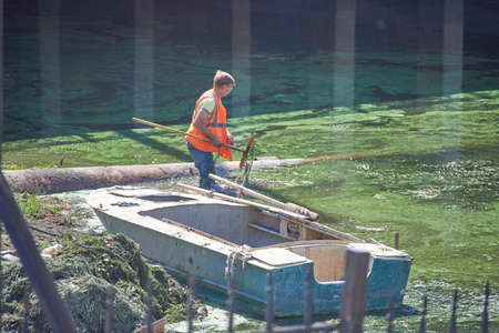 Astrakhan, Russia - 08.12.2020: A man in an orange signal vest clears mud from the river. There is a...