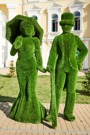 Astrakhan, Russia - 09.18.2020: Topiary sculpture of lady with umbrella and dressed in flared skirt and jentleman with a cane and a top hatのeditorial素材