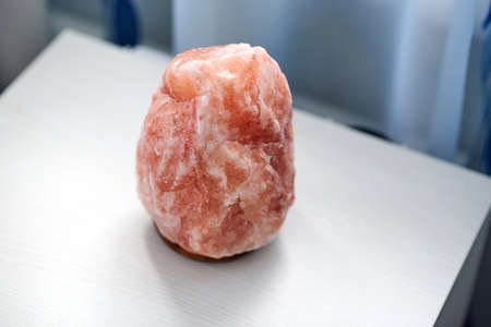 An orange salt lamp stands on a white bedside tableの写真素材