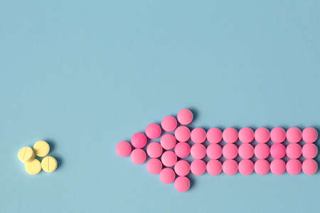 Pink and yellow pills as a pointer on a blue background