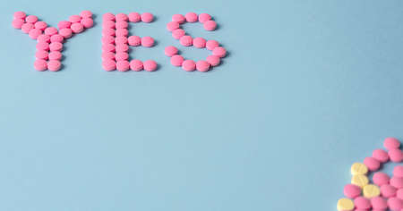 word YES is made up of pink pills on a blue background