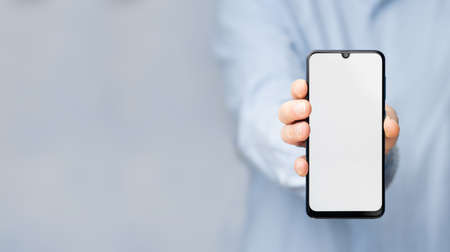 Man's hand in a blue shirt holding smartphone with blank screen. Take your screen to put on advertisingの写真素材