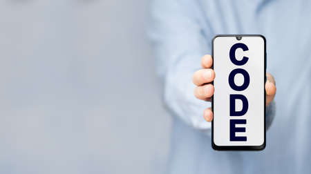 Man's hand in a blue shirt holding smartphone with text CODE on a blue backgroundの写真素材