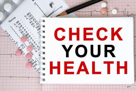 Notebook page with text CHECK YOUR HEALTH on a table with a pills and pencil, medical concept, top viewの写真素材