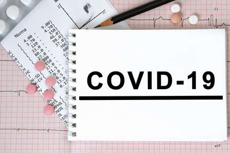Notebook page with text COVID-19 on a table with a pills and pencil, medical concept, top viewの写真素材