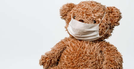 Teddy bear toy is sitting in white medical mask on a white background. Concept of illness, hygiene and virus protection for childrenの写真素材