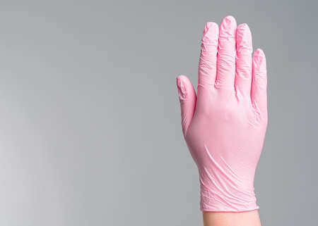 Close-up doctor's hand in pink rubber gloves shows a stop gesture on gray background.の写真素材