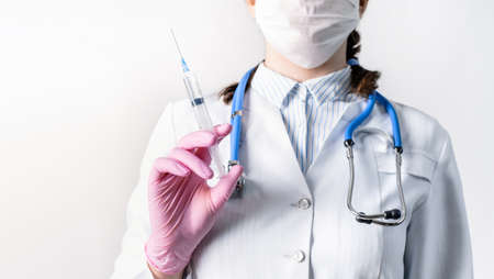 Cropped view of young female doctor in a white coat, in a medical mask and pink sterile gloves hold syringe. Focus at syringe. Vaccination concept.の写真素材