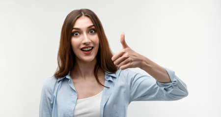 Happy caucasian Young female with long chestnut hair, dressed in casual clothes, shows OKAY sign with both hands, demonstrates approval, isolated over white background.の写真素材