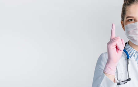 Cropped view of young beautiful woman doctor in a white coat and pink sterile gloves shows a sign...