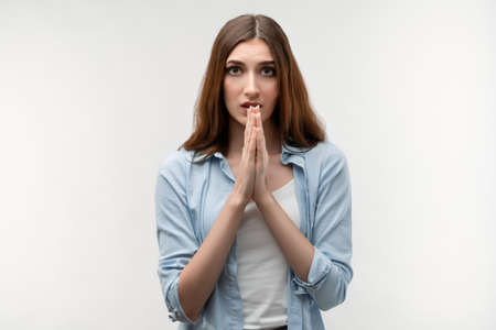 Young female with long chestnut hair holds hands in namaste sign. Meditates indoors, praying for peace and love, having calm and peaceful facial expression. Relaxation conceptの写真素材