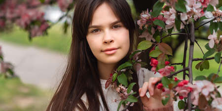 Closeup beautiful young brunette girl 11-12 years under the flowering pink tree, lifestyleの写真素材