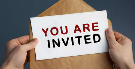 Cropped view of man holding craft envelope with text YOU ARE INVITED on blue background, conceptの写真素材