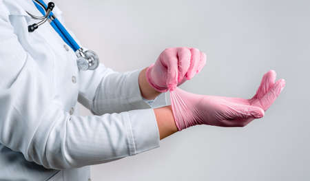 Female doctor's hands putting on pink sterile gloves isolated on gray background, medical conceptの写真素材