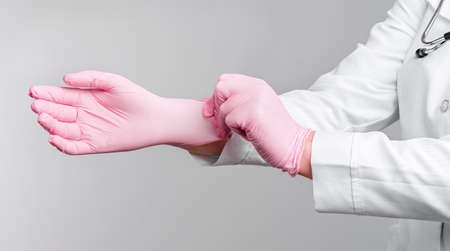Female doctor's hands putting on pink sterile gloves isolated on gray background, medical conceptの写真素材