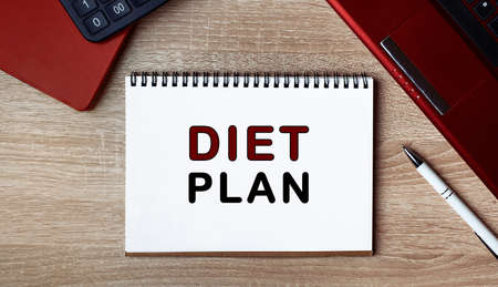 Notebook with text DIET PLAN. Notebook on desk with laptop and a pen. Top view, conceptの写真素材