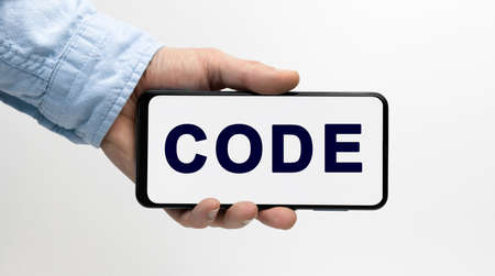Man's hand holding smartphone with text CODE on white background, conceptの写真素材