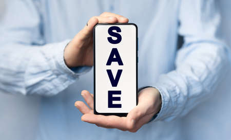 Man's hands in a blue shirt holding smartphone with text SAVE, conceptの写真素材