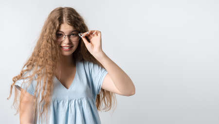 Portrait of charismatic modern girl with curly long hair in casual light clothes and wears round...