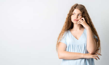 Photo of Pensive European young woman with curly long hair, looking up having pensive expression. Isolated over white background. Copy space for your textの写真素材