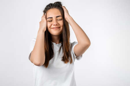 Pretty carefree modern girl with long chestnut hair holding to her head or touching hair. Isolated on white background. Emotions, expressions, hairstyle and people concept.の写真素材