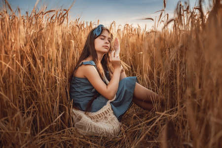 Portrait of Little girl 10-12 years old with long brown hair, walk in a wheat field on a summer evening. Image with selective focus, toning and noiseの写真素材