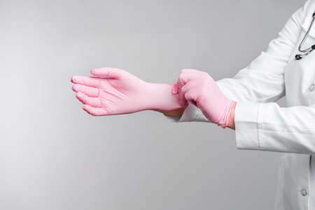 Female doctor's hands putting on pink sterile gloves isolated on gray background, Medical conceptの写真素材