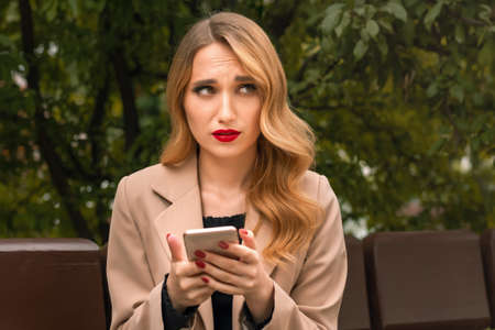 Young blonde woman is sitting on a Park bench and waiting for a phone call from her boyfriend....