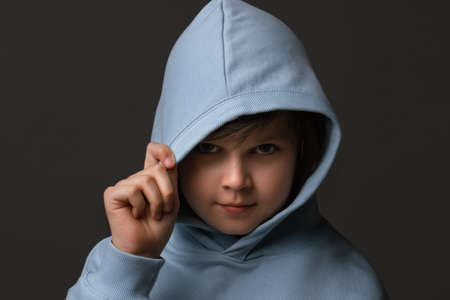 Portrait of Cute boy 10-12 years old, dressed in casual clothes, standing with a hood on his head and looking at camera on gray studio backgroundの写真素材