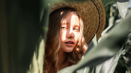 Stylish young girl 10-12 years old in vintage clothing and straw hat posing in a cornfield. Unity with nature. Caring for the environment, calm moment in countrysideの写真素材
