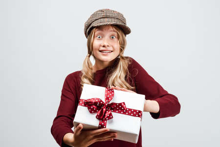 Beautiful blonde girl 10-12 years old dressed in casual sweater, holding gift box. Studio shot,...