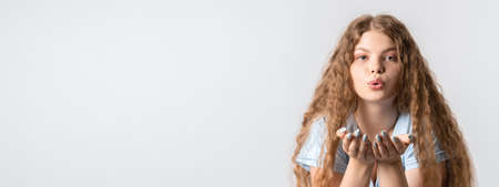 Beautiful European young woman with curly long hair makes air kiss, blows over two palms, wants to...