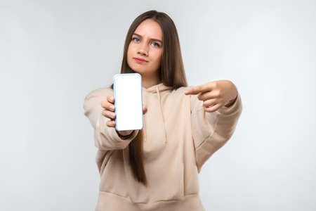 Portrait of pretty girl with long chestnut hair, dressed in casual clothes, pointing finger at blank...